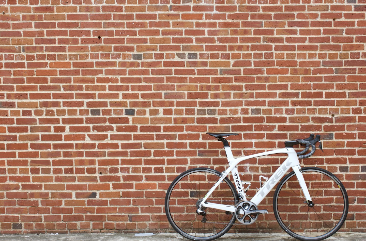 Una bicicletta da corsa bianca appoggiata a un muro di mattoni rossi.